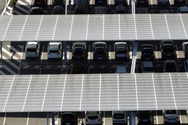 Güneş panellerinin hava görüntüsü park yerinin üzerine gölge çatısı olarak yerleştirilmiş ve temiz elektriğin etkin üretimi için park edilmiş arabalar var. Fotovoltaik teknoloji şehir altyapısına entegre edildi.