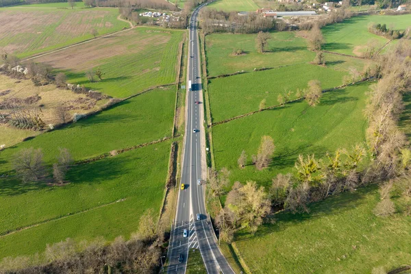Aerial view of intercity road between green agricultural fields with fast driving cars. Top view from drone of highway traffic.
