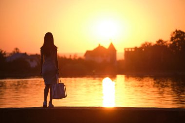 Sıcak bir akşamda göl kıyısında tek başına duran yalnız bir kadın. Yalnızlık ve doğa konseptinde rahatlama..