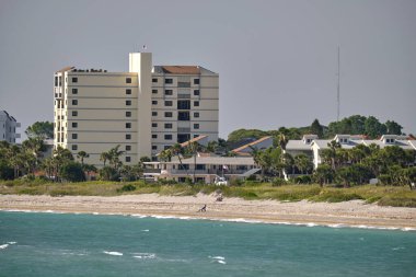 Beyaz kumları, mavi suları, yüksek otel binaları olan bir tatil köyü. Mutlu insanlar güneşleniyor ve okyanusta yüzüyor..