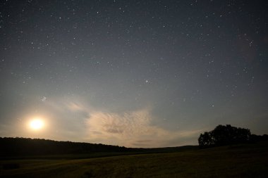 Beautiful panorama of bright blue sky with shining stars and milkyway over dark mountains landscape at night.