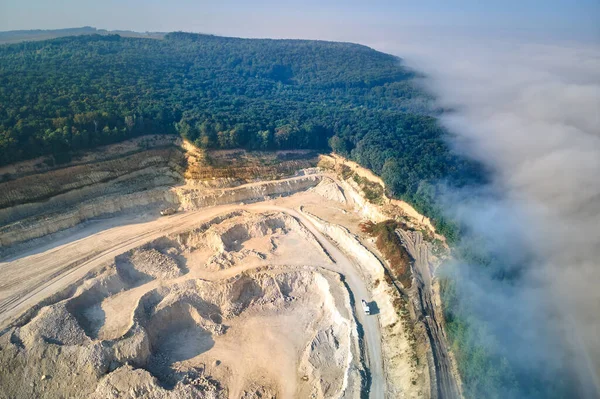 Aerial view of open pit mining of limestone materials for construction industry with excavators and dump trucks.