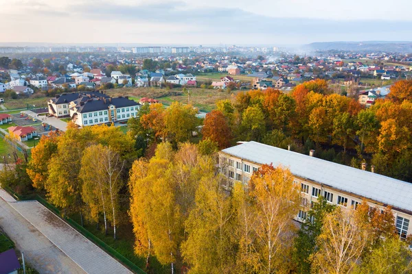 Aerial view of school, college or kindergarten building with big yard among autumn trees on rural landscape background.
