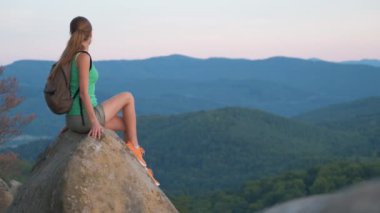 Kayalık dağ yamacında tek başına oturan kadın doğa manzarasının tadını çıkarıyor. Aktif yaşam konsepti.