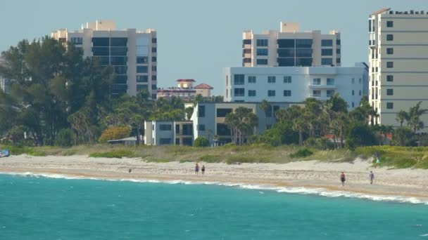 白い砂 青い水 背の高いホテルの建物とリゾートビーチ 海で日光浴や水泳をする幸せな人々 — ストック動画