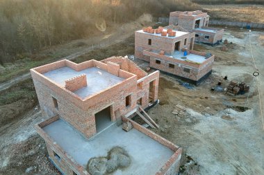 Kenar mahallelerde inşaat halindeki tuğla iskelet duvarları olan yeni evlerin havadan görünüşü. Modern şehir banliyölerinde gayrimenkul geliştirme.