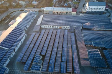 Sanayi binasının çatısına yeşil ekolojik elektrik üretmek için monte edilmiş mavi fotovoltaik panelli güneş enerjisi santralinin hava görüntüsü. Sürdürülebilir enerji konsepti üretimi.