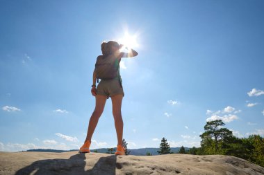 Sportive woman walking alone on hillside trail. Female hiker enjoying view of summer nature from rocky cliff on wilderness path. Active lifestyle concept.