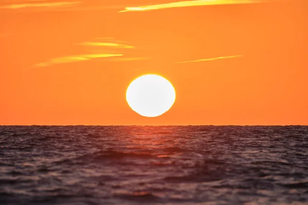 Ocean sunset. Big white sun on dramatic bright sky background, soft evening cloud over sea dark water.