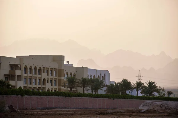 Sunset landscape with remote hotel complex against dark mountain peaks in egyptian desert.