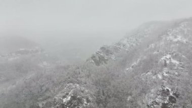 Soğuk ve sakin bir günde, şiddetli kar yağışı sırasında dağlardaki kayalıklarla kaplı sisli hava manzarası..