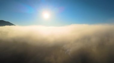 Ufuktaki dağ tepelerinin uzak karanlık siluetleri ile beyaz yoğun sis üzerinde renkli gün doğumunun havadan görüntüsü.