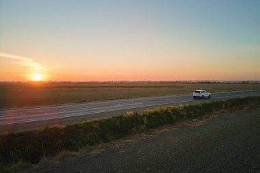 Gün batımında hızlı giden bulanık arabalı şehirlerarası yol manzarası. Akşamları otoban trafiğinin insansız hava aracı görüntüsü.