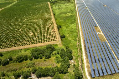 Aerial view of sustainable electric power plant between agricultural farm fields with solar photovoltaic panels for producing clean electrical energy. Renewable electricity with zero emission concept.