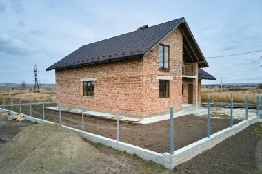 Tuğla duvarları ve ahşap çatı iskeleti inşaat halindeki metalik fayanslarla kaplı bitmemiş evin havadan görüntüsü..