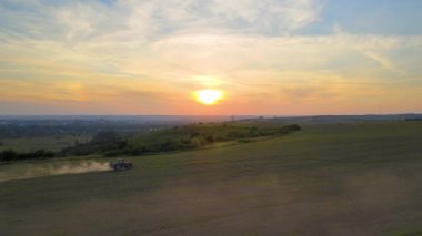 Gün batımında tarım sahasında böcek öldürücü kimyasallar püskürten traktör..