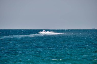 Mavi deniz suyunun dalgalı yüzeyi ve durgun dalgalarda hızlı yüzen beyaz sürat teknesiyle deniz manzarası..