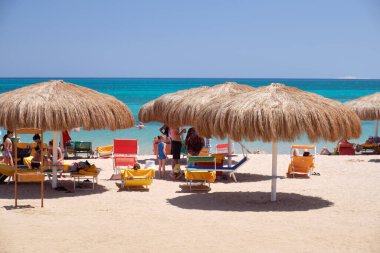 Yazın mavi renkli gökyüzüne karşı dinlenen güneşli deniz kıyılarında saman gölgesi şemsiyeleri..