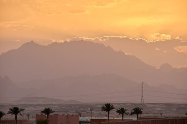 Uzak otel kompleksiyle gün batımı manzarası Mısır çölündeki karanlık dağ zirvelerine karşı.