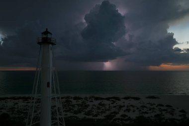 Deniz kıyısındaki uzun deniz feneri fırtınalı bir gecede ticari gemilerin seyrüsefer için yanıp sönen ışık. Okyanus üzerinde şimşekler çakan fırtına gemiler için tehlike arz ediyor..