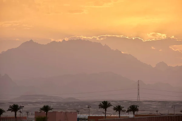 Sunset landscape with remote hotel complex against dark mountain peaks in egyptian desert.