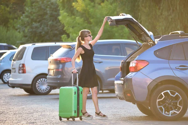Young woman driver taking out suitcase bag out of her car. Travelling and vacations concept.