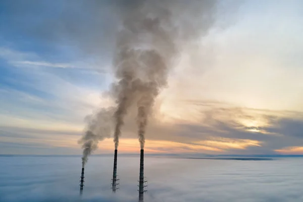 Aerial view of coal power plant high pipes with black smoke moving up polluting atmosphere at sunset.