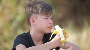 Genç yakışıklı delikanlı olgun muz yiyor yaz günü açık havada atıştırıyor..