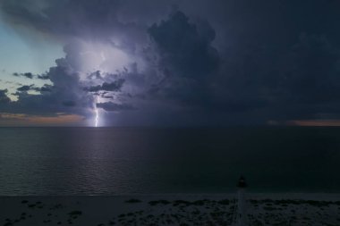 Deniz kıyısındaki uzun deniz feneri fırtınalı bir gecede ticari gemilerin seyrüsefer için yanıp sönen ışık. Okyanus üzerinde şimşekler çakan fırtına gemiler için tehlike arz ediyor..