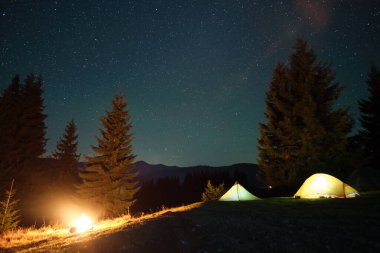 Parlak turist çadırları, gece gökyüzünün altındaki karanlık dağlarda, parlayan yıldızlarla parlayan kamp alanlarında. Etkin yaşam tarzı kavramı.