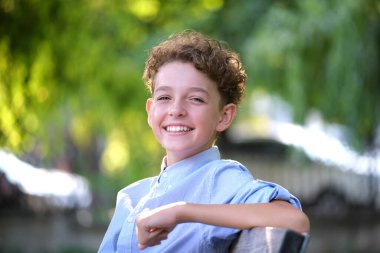 Genç mutlu çocuk yaz parkında bankta rahatlıyor. Yazın dışarıda eğlenen pozitif çocuk. Çocuk esenliği kavramı.