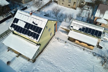 Aerial view of house roof with solar panels covered with snow melting down in winter end for producing clean energy. Concept of low effectivity of renewable electricity in northern region.