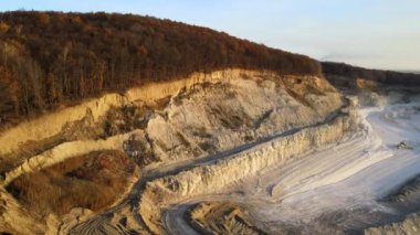Kazı makineleri ve çöp kamyonlarıyla inşaat endüstrisi için kumtaşı malzemelerinden oluşan açık maden manzarası. Madencilik ve kullanışlı mineral üretiminde ağır ekipman.