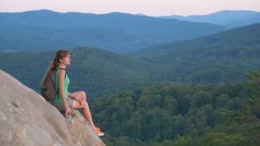 Yürüyüşçü kadın kayalık dağın tepesinde dinleniyor ve vahşi doğa yolculuğunun tadını çıkarıyor. Yüksek tepe yolundan geçen yalnız bir kadın gezgin. Sağlıklı yaşam tarzı kavramı.