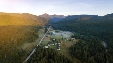 Sonbahar gündoğumunda dağ ormanları ve karanlık tepeler arasındaki küçük kırsal evlerin üzerinde parlak sisli bir sabah manzarası. Şafak vakti vahşi ormanın güzel manzarası.