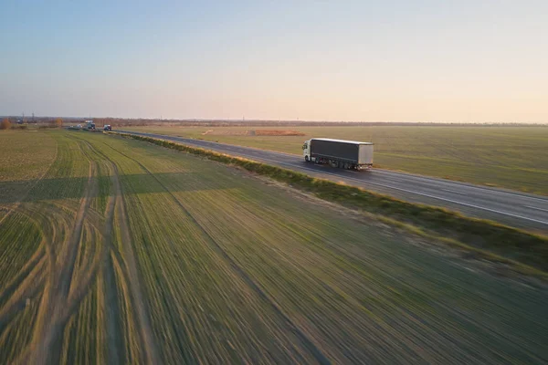 Aerial view of semi-truck with cargo trailer driving on highway hauling goods in evening. Delivery transportation and logistics concept.