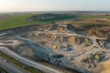 Kazı makineleri ve çöp kamyonlarıyla inşaat endüstrisi için kumtaşı malzemelerinden oluşan açık maden manzarası. Madencilik ve kullanışlı mineral üretiminde ağır ekipman.