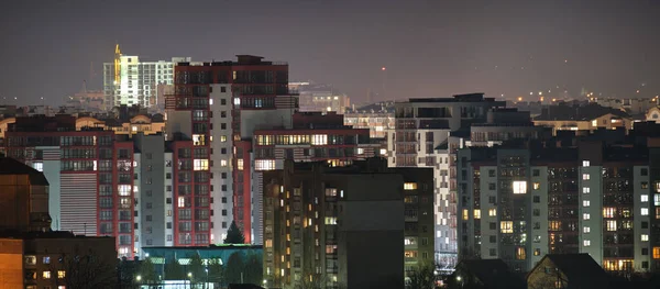 Architectural details of modern high apartment buildings with many illuminated windows and balconies at night.