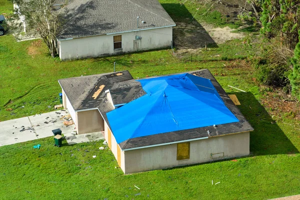 Top view of leaking house roof covered with protective tarp sheets against rain water leaks until replacement of asphalt shingles. Damage of building rooftop as aftermath of hurricane Ian in Florida.