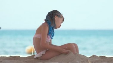 Cute happy child girl playing with sand on ocean beach during summer tropical vacations.