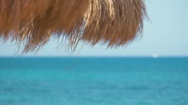 Tropik tatil beldesindeki deniz kenarındaki saman gölgesi şemsiyelerinin ayrıntıları. Yaz tatilleri ve kaçış konsepti.