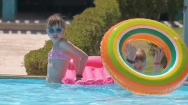 Happy children brother and sister playing on inflatable air mattress in swimming pool on sunny summer day during tropical vacations. Summertime activities concept.