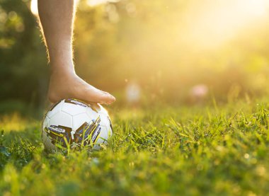 Ayakkabısız bir erkek ayak çimenli bir alanda futbol topunda güneş ışığı ve fotokopi alanı ile.