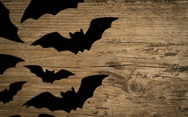 Gri ahşap bir zemin üzerinde büyük ve küçük siyah yarasalar. 
