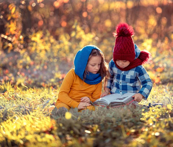 Niños niño y niña leen un libro juntos mientras están sentados en la hierba en la naturaleza en el parque —  Fotos de Stock