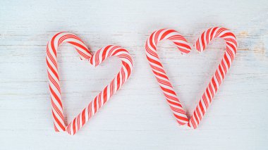Beyaz ahşap arka planda çizgili kırmızı-beyaz lolipoplardan yapılmış kalpler.