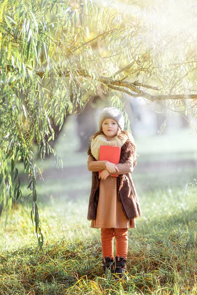 Dziewczyna z czerwoną książką stoi pod drzewem. — Zdjęcie stockowe