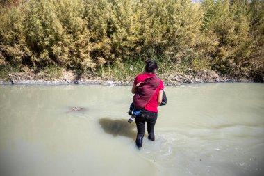 10-22-2021 Honduraslı kadın, Meksika ve ABD arasındaki doğal sınır olan Rio Bravo 'yu geçerken 4 yaşındaki oğlunu sırtında taşıyor ve insani sığınma talebinde bulunuyor.