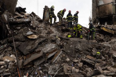 İtfaiyeciler ve kurtarma ekipleri bir Rus füzesi tarafından yıkılan bir binanın enkazını temizliyor.