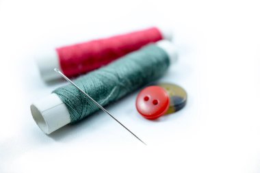 Çeşitli renklerdeki dikiş iplikleri, dikiş iğneleri ve beyaz arkaplanda izole edilmiş gömlek düğmeleri.
